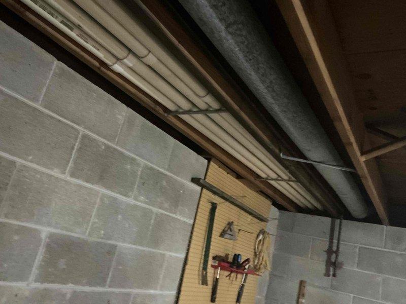 Conducted inspection of utility area revealing significant corrosion and oxidation on copper pipes in HVAC/plumbing system mounted beneath floor joists. Observed deterioration particularly severe at elbow joints, with visible rust compromising system integrity. Recommended complete replacement of affected copper piping and integration with existing PVC components to prevent potential leaks and system failure.