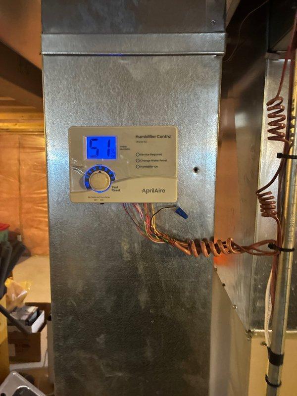 Installed and configured an AprilAire humidifier system with digital control panel displaying current humidity level (51%). The control unit was mounted on the HVAC system with proper wire connections (yellow, red, and blue) established. System includes "Service Required" and "Humidifier On" indicator functionality and was properly integrated with the existing furnace and ductwork in the basement utility area.