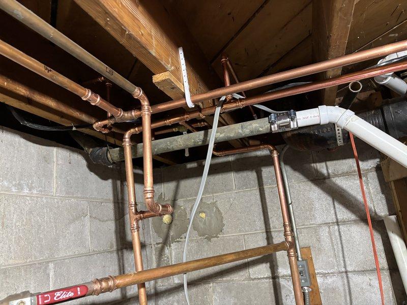 Inspected extensive copper supply line and PVC drainage system in unfinished basement area. Documented the condition of the plumbing infrastructure, noting some aging and discoloration on copper pipes. Verified proper installation of waste stack with supporting clamps and confirmed all connections were secure with no active leaks.