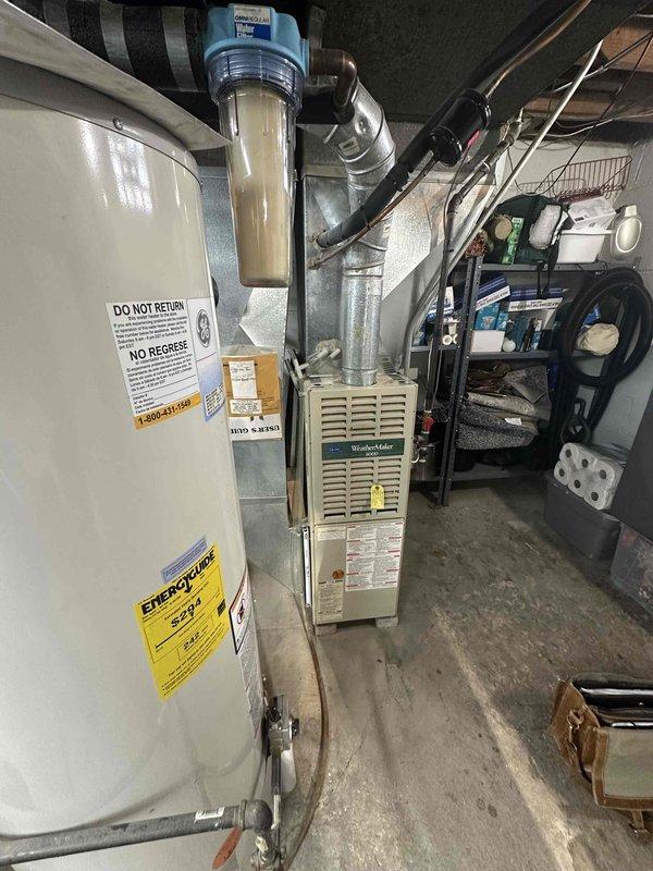 Completed inspection of residential HVAC system located in basement utility area. Documented existing furnace (WeatherMaker model) with connected ductwork, adjacent water heater, and water filtration system. Prepared estimate for complete system replacement due to age and condition of current equipment.