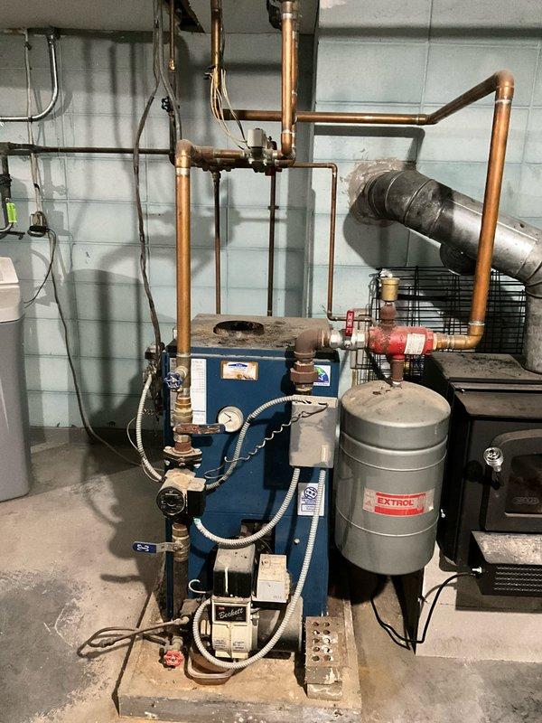 Conducted comprehensive assessment of aging hydronic heating system featuring blue boiler unit with EXTROL expansion tank and extensive copper piping network showing signs of wear. Documented current configuration including valve placement, pressure gauges, and connection points to develop appropriate replacement options. Photographed mechanical room setup for accurate system specifications and interface requirements with existing ductwork and water circulation components.