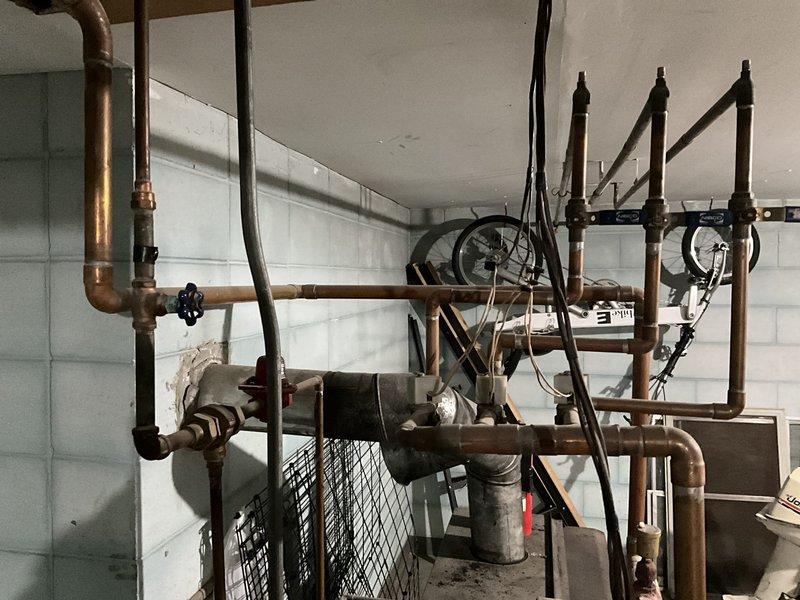 Conducted comprehensive assessment of aging hydronic heating system featuring blue boiler unit with EXTROL expansion tank and extensive copper piping network showing signs of wear. Documented current configuration including valve placement, pressure gauges, and connection points to develop appropriate replacement options. Photographed mechanical room setup for accurate system specifications and interface requirements with existing ductwork and water circulation components.