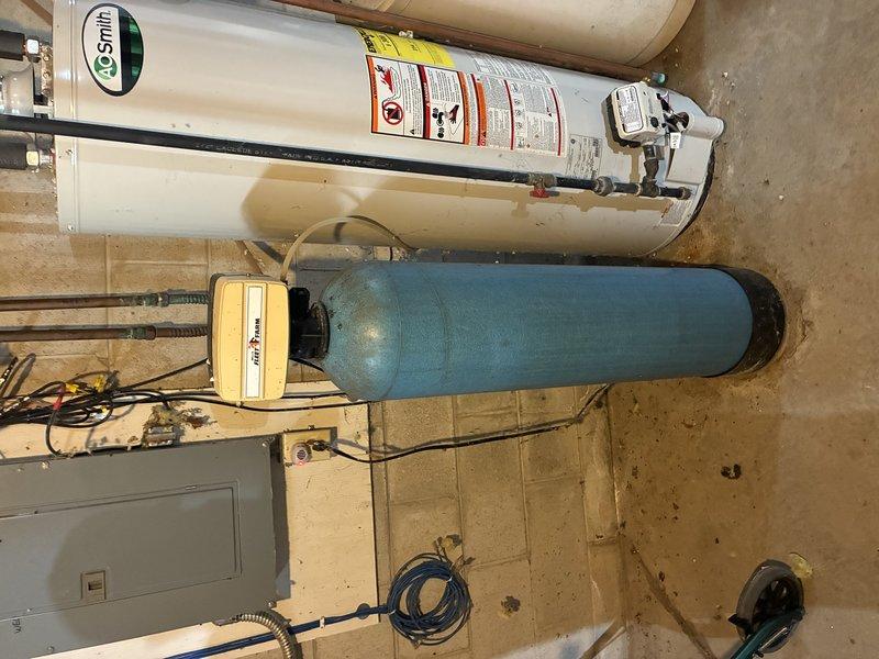 Inspected and documented A.O. Smith water heater installation with accompanying blue expansion tank in utility area. System features copper piping connections, standard electrical components, and proper safety labeling. Secondary filtration or water softening system observed adjacent to the main unit, all installed on tile flooring with appropriate wall-mounted electrical panel connections.
