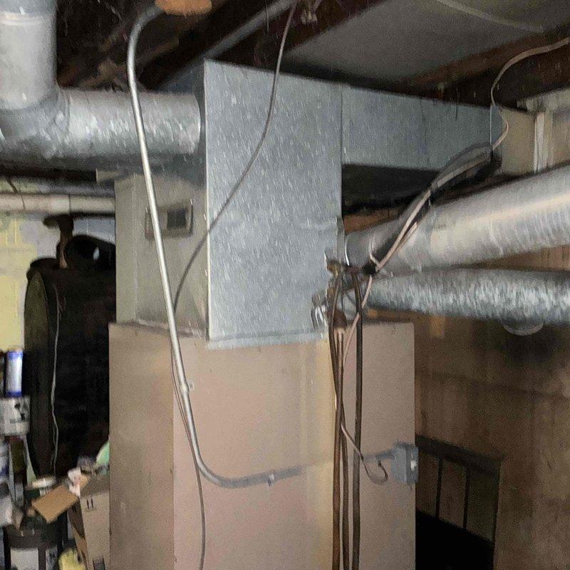 Conducted assessment of an aging HVAC system with identified outdoor condenser unit showing significant snow accumulation and potential exposure damage. Inspection of basement utility room revealed outdated furnace with deteriorating ductwork connections. Recommended full system replacement to improve energy efficiency and prevent potential failure during extreme weather conditions.