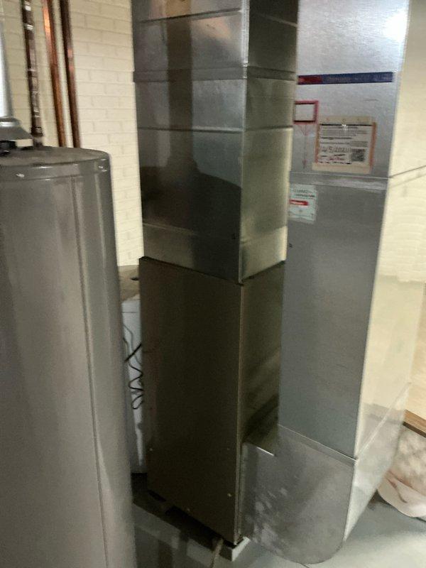 Conducted inspection of existing HVAC system in basement utility room, including furnace unit with vertical configuration and adjacent water heater. Examined plumbing infrastructure consisting of PVC drainage pipes and red supply lines mounted to ceiling joists, providing client with replacement options based on assessment findings.