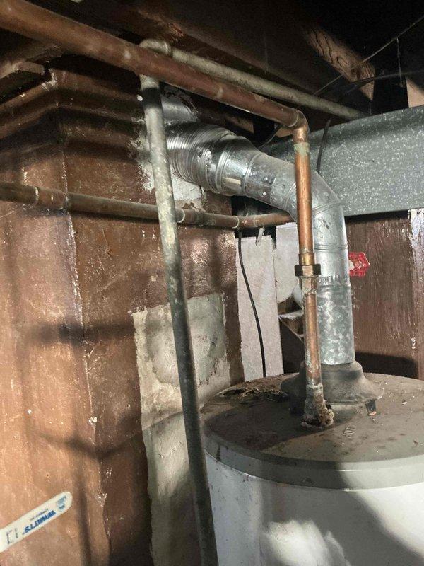 Conducted assessment of aging water heater installation in basement utility area showing signs of galvanic corrosion at copper/galvanized pipe connections. Noted significant water damage on concrete floor and walls, with visible staining and moisture issues. Recommended replacement of current system with modern unit to address corrosion issues and prevent potential water damage progression.