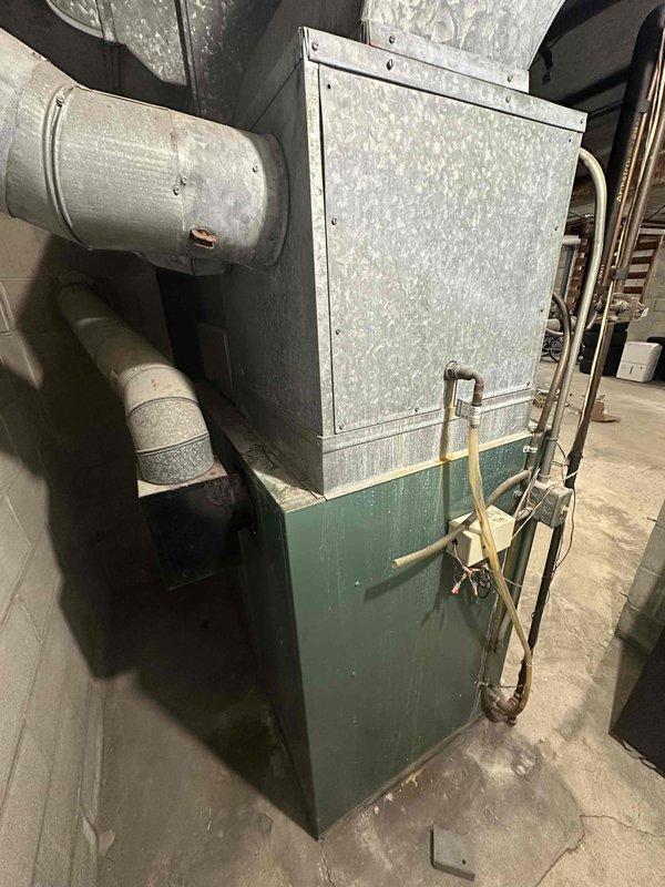 Conducted comprehensive inspection of aging HVAC system showing signs of normal wear in basement/utility area. Documented exterior conditions including weathered wall surfaces with moisture damage and evaluated existing connections to ductwork, drainage lines, and utility access points. Recommended complete system replacement due to age and efficiency concerns.