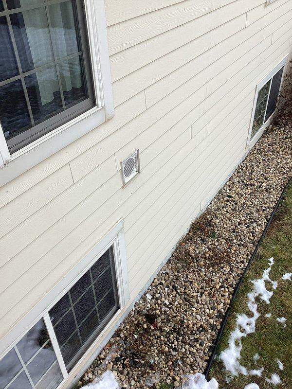 Completed exterior inspection of vent terminations on client's property. Observed standard metal vent cover with mesh grid showing minor dirt/mildew accumulation around base. Verified proper installation and positioning of all exterior ventilation components including the primary exhaust outlet mounted in the siding wall.