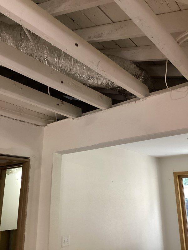 Completed installation of insulated cylindrical metal ductwork in exposed ceiling area, properly securing between wooden joists during ongoing renovation. System was carefully integrated with existing electrical components while maintaining proper clearances in the construction zone.