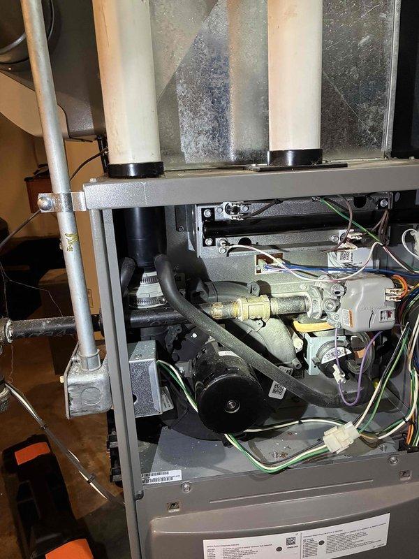 Performed diagnostic inspection on residential furnace system, opening access panels to examine internal components including motor assembly, control boards, and gas valve connections. Observed normal dust accumulation and wear on components consistent with regular operation. System appears properly installed with PVC exhaust venting and appropriate ductwork connections.