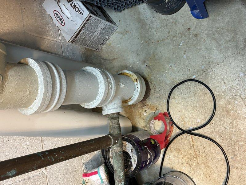 Conducted thorough assessment of basement plumbing infrastructure, documenting water supply system components including PVC piping configuration with multiple joints and fittings. Evaluated condition of T-junction pipe assembly and rubber coupling with metal band clamps securing vertical drainage sections. Verified integrity of all connection points and mounting hardware where pipes are secured to concrete wall structure.