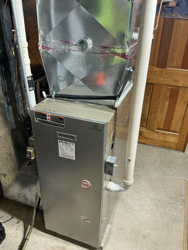 Completed installation of a Payne furnace unit in utility/mechanical room, replacing aging HVAC system. New installation includes properly connected PVC ventilation pipes, sealed ductwork connections with metallic tape, and verified operational status as indicated by system indicator light.