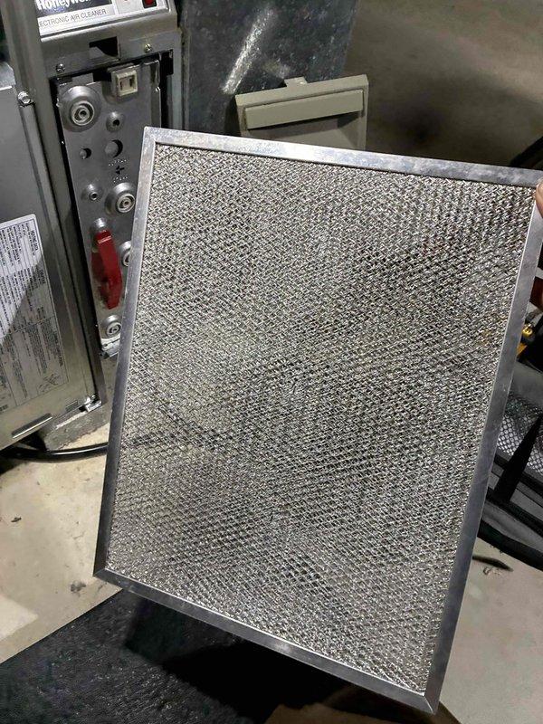 Performed routine HVAC tune-up service including inspection of filtration system and electrical diagnostics. Examined metallic air filter for accumulated particulates and measured system voltage parameters (56.89V) using Fieldpiece SC680 multimeter with thermocouple probes. System operational within normal parameters after service completion.