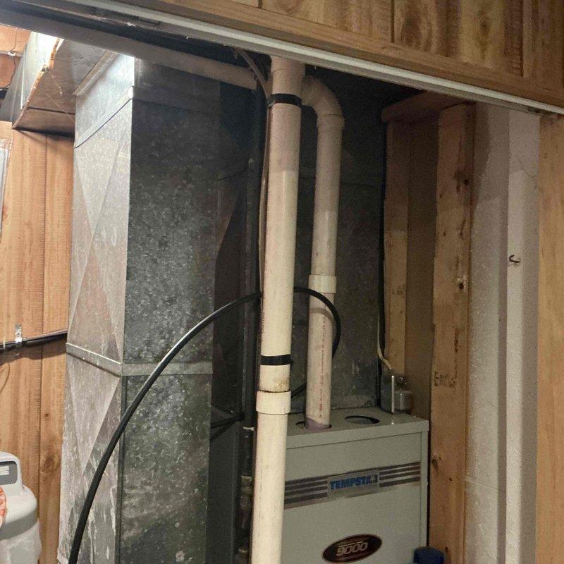Conducted inspection of existing home heating system located in basement utility area. Verified installation of Tempstar/Heil furnace with proper metal ductwork connections and PVC intake/exhaust venting secured with appropriate strapping. Examined surrounding plumbing infrastructure including copper and PVC piping systems for potential integration issues. System appears properly installed with all components functional.