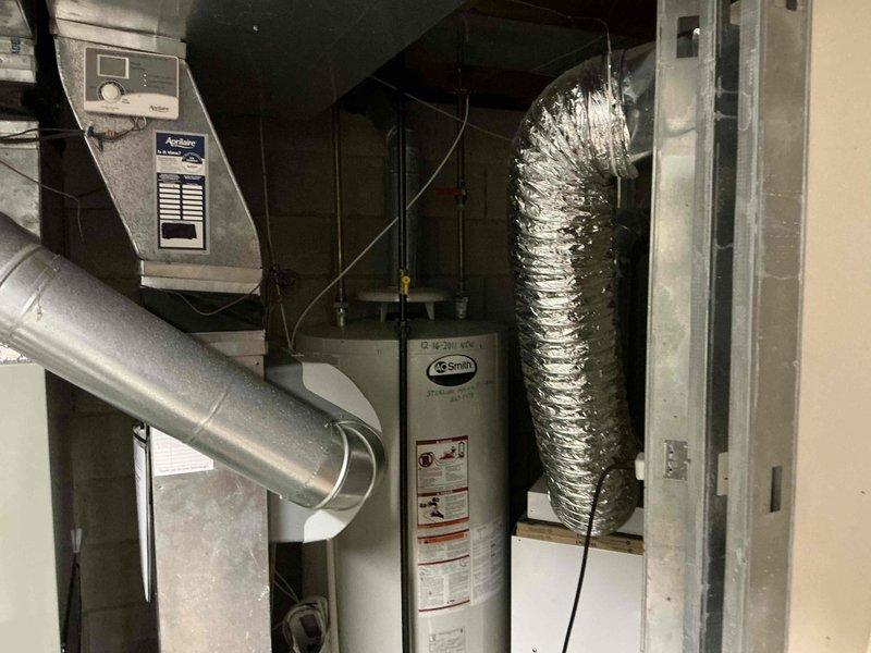 Conducted inspection of existing water heating system, which included an A.O. Smith water heater (installed 12-16-2011) and associated copper piping connections. Noted G Smith equipment in utility room with connected ductwork and HVAC control unit. Documentation included photographic evidence of current installation configuration for replacement estimation purposes.