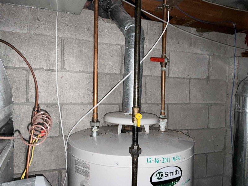 Conducted inspection of existing water heating system, which included an A.O. Smith water heater (installed 12-16-2011) and associated copper piping connections. Noted G Smith equipment in utility room with connected ductwork and HVAC control unit. Documentation included photographic evidence of current installation configuration for replacement estimation purposes.