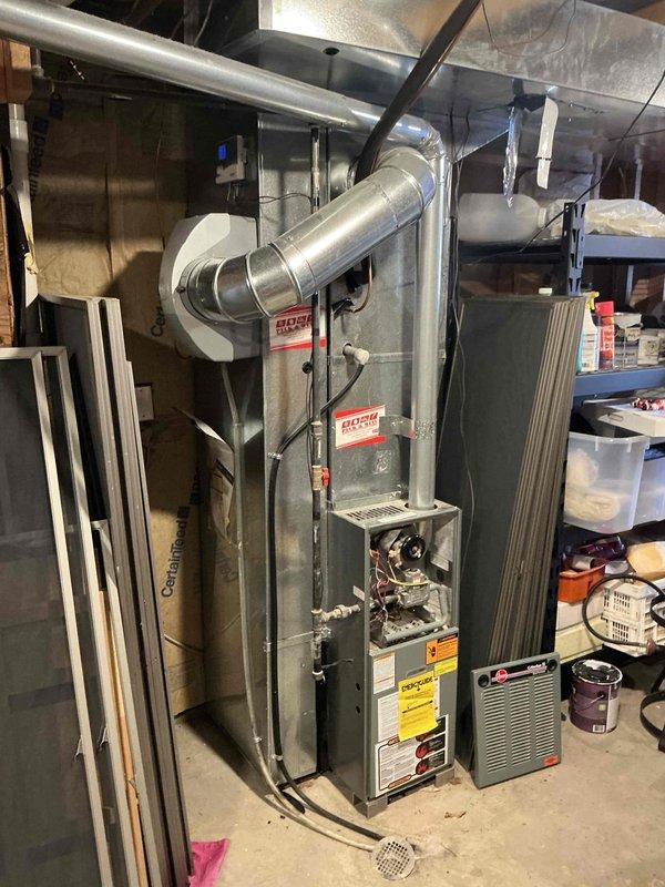 Completed installation of a Bosch HVAC system in residential basement setting, including furnace unit with proper gas line connection and ventilation. System features integrated ductwork with both round and rectangular sections, and all electrical components were properly wired and tested for optimal performance. Installation meets all safety requirements with appropriate floor drainage system in place.