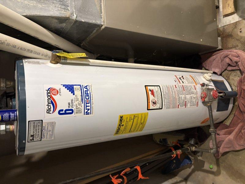 Inspected Richmond Integra water heater system in utility area. Documented unit condition including connections, pressure relief valve, and pipe fittings. Applied lubricant to pipe connection (WD-40) as part of routine maintenance to ensure proper function and prevent leakage.