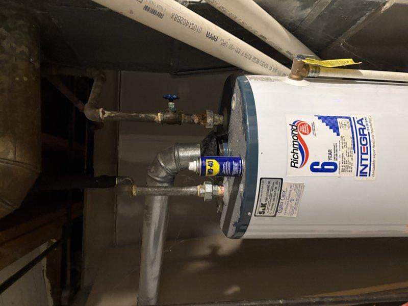 Inspected Richmond Integra water heater system in utility area. Documented unit condition including connections, pressure relief valve, and pipe fittings. Applied lubricant to pipe connection (WD-40) as part of routine maintenance to ensure proper function and prevent leakage.