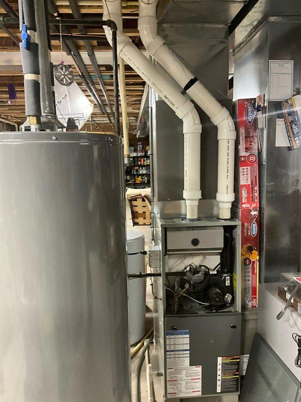 Completed HVAC system replacement in customer's utility room, installing a new Trane XR80 furnace with proper PVC venting secured to ceiling joists. System includes digital thermostat/control panel mounted adjacent to the furnace unit with all electrical connections properly wired and tested for optimal performance.