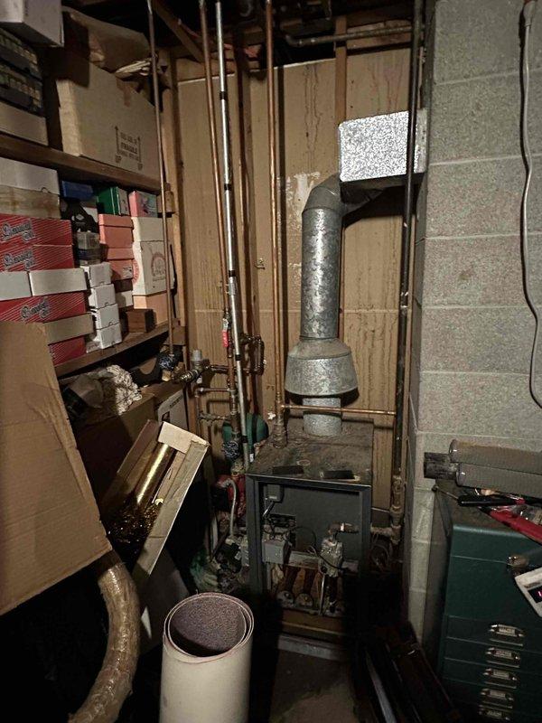 Conducted assessment of existing boiler system in basement utility area. Observed aging green boiler unit with functioning digital display. System includes extensive copper piping network and metal flue with elbow joint. Recommended replacement due to observed inefficiency and age-related deterioration.