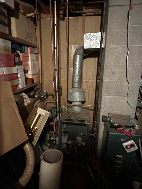 Conducted assessment of existing boiler system in basement utility area. Observed aging green boiler unit with functioning digital display. System includes extensive copper piping network and metal flue with elbow joint. Recommended replacement due to observed inefficiency and age-related deterioration.