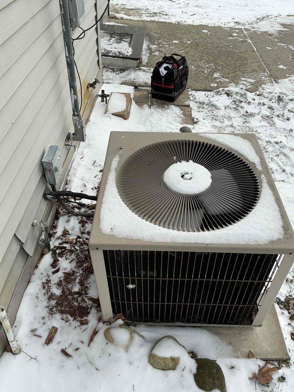 Conducted inspection of existing HVAC system showing significant deterioration. Outdoor air conditioning unit exhibited snow accumulation on fan grille with adjacent corroded water heater connections. Recommended full system replacement due to extensive corrosion observed on water heater pipes and visible rust at critical connection points, indicating imminent system failure risk.