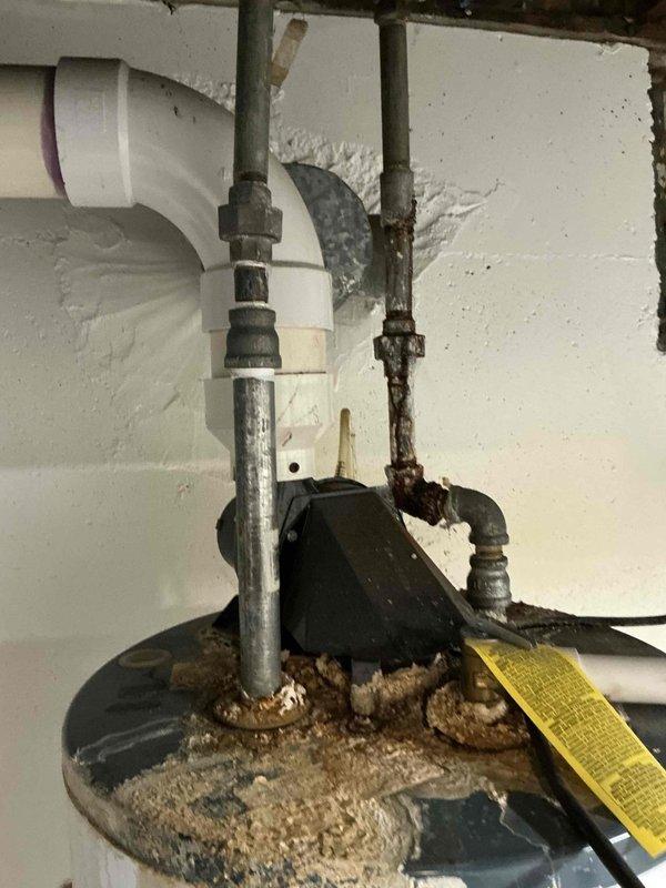 Conducted inspection of existing HVAC system showing significant deterioration. Outdoor air conditioning unit exhibited snow accumulation on fan grille with adjacent corroded water heater connections. Recommended full system replacement due to extensive corrosion observed on water heater pipes and visible rust at critical connection points, indicating imminent system failure risk.