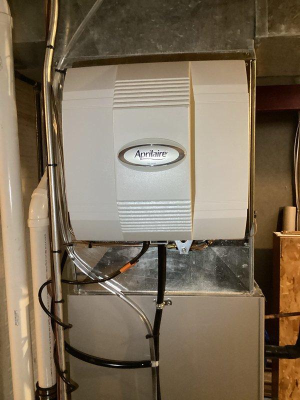 Successfully installed new high-efficiency furnace with digital thermostat display showing proper operation at 26 degrees. Mounted Aprilaire whole-home humidifier on the system, connecting all necessary tubing and ensuring proper integration with the HVAC system. Applied service identification sticker with 24-hour service contact information for future reference.