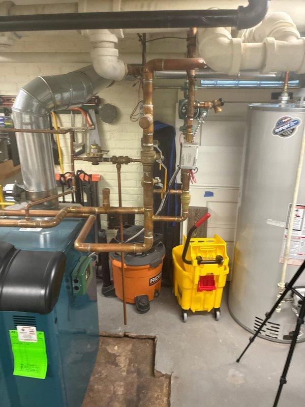 Conducted comprehensive inspection of existing blue-green boiler system in utility room basement. Documented extensive copper piping network, brass valves, and circulation pump. Evaluated connection points to water heater and PVC drainage/ventilation components. Photos taken for documentation and future reference.