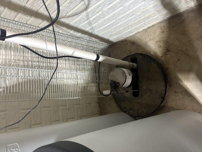 Conducted inspection of existing sump pump installation in basement. System includes circular basin with black lid, PVC discharge piping connected to drainage system, and visible electrical connections. Assessed condition of surrounding concrete floor and moisture barriers on foundation walls. Provided estimate for recommended upgrades to improve basement flood protection.