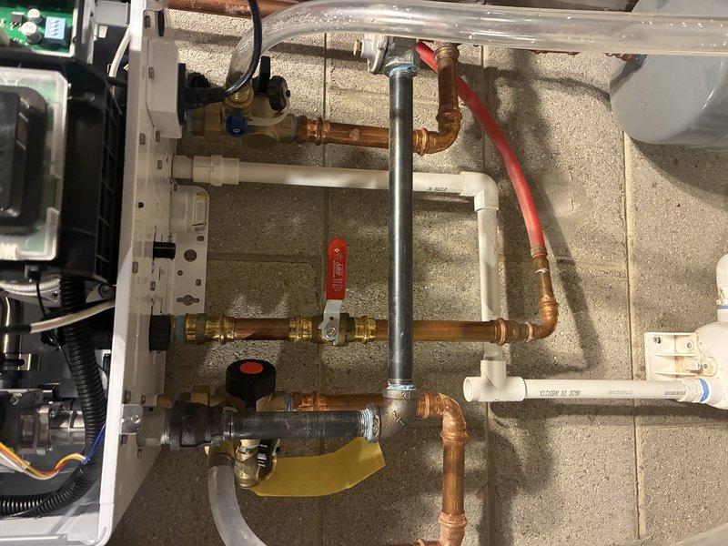 Conducted comprehensive inspection and evaluation of a complex mechanical system featuring interconnected copper and PVC piping network. Identified and documented the control unit with digital display panel, multiple valves including prominent red shutoff valve, and associated electronic components. System appears well-maintained with professional connections and proper mounting against concrete/textured wall.