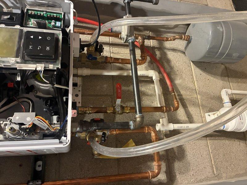 Conducted comprehensive inspection and evaluation of a complex mechanical system featuring interconnected copper and PVC piping network. Identified and documented the control unit with digital display panel, multiple valves including prominent red shutoff valve, and associated electronic components. System appears well-maintained with professional connections and proper mounting against concrete/textured wall.