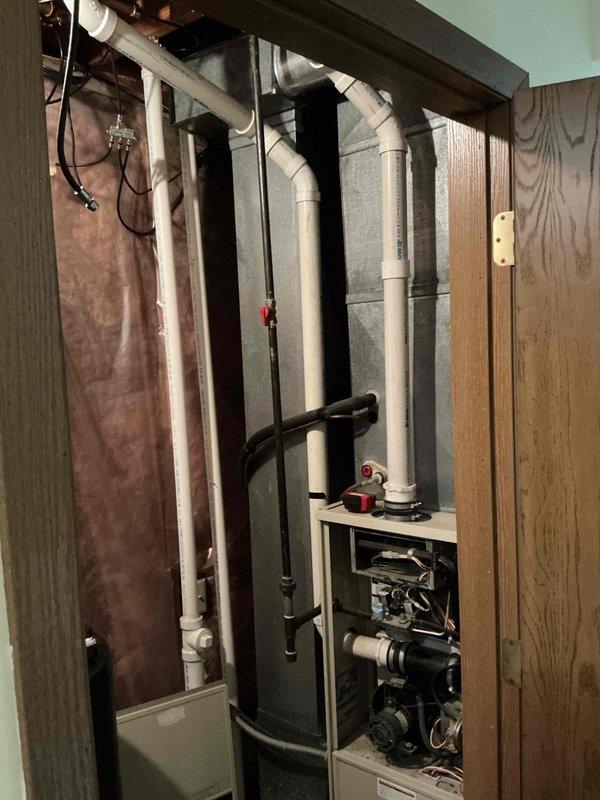 Completed assessment and photo documentation of residential HVAC system replacement needs, focusing on the existing furnace unit with exposed control board and motor assembly. Inspected current installation configuration including PVC venting, refrigerant lines, and integration with existing ductwork in the utility closet, noting the condition of surrounding plumbing infrastructure.