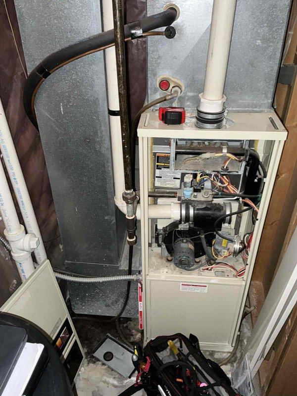 Completed assessment and photo documentation of residential HVAC system replacement needs, focusing on the existing furnace unit with exposed control board and motor assembly. Inspected current installation configuration including PVC venting, refrigerant lines, and integration with existing ductwork in the utility closet, noting the condition of surrounding plumbing infrastructure.