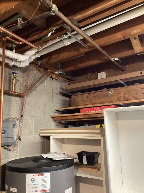 Performed inspection and documentation of plumbing infrastructure in unfinished basement utility area. Examined copper piping system including valve connections and control components. Verified proper installation of water heater/tank and noted all visible plumbing runs through ceiling joists (copper and PVC) were in serviceable condition.