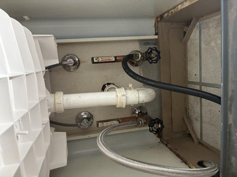 Inspected tank water heater installation with visible valves, supply lines, and connections. Observed normal wear on valve handles with some tarnishing. System appears functional with properly installed PVC piping, flexible braided supply lines, and appropriate shut-off valves all in working condition.