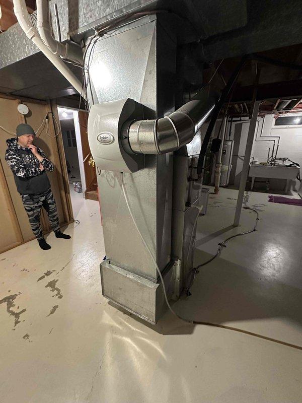 Inspected unfinished basement area and completed installation of a new Carrier air handler unit. System features silver/light gray finish with integrated curved metallic ductwork connections. Verified proper placement of unit against concrete block wall and ensured all utility connections were properly secured to existing building infrastructure within the mechanical area.