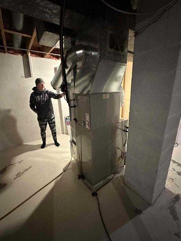 Inspected unfinished basement area and completed installation of a new Carrier air handler unit. System features silver/light gray finish with integrated curved metallic ductwork connections. Verified proper placement of unit against concrete block wall and ensured all utility connections were properly secured to existing building infrastructure within the mechanical area.