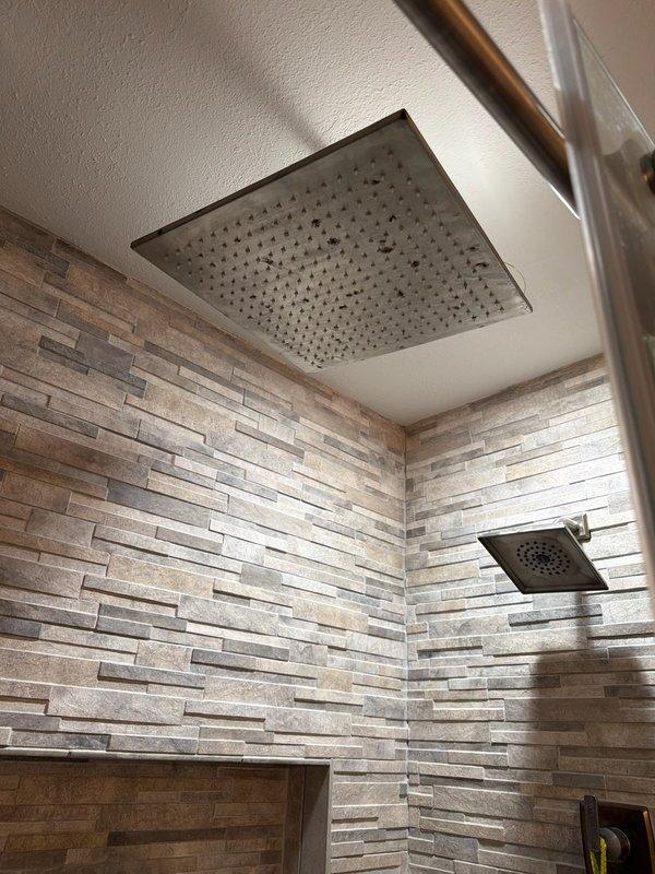 Inspected bathroom fixtures including toilet installation with proper water supply connection and a shower system equipped with dual showerheads. Noted some mineral buildup on the rainfall showerhead that may require future maintenance. All plumbing connections appear secure and functional.