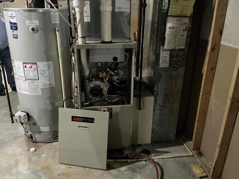 Completed visual inspection of existing Lennox furnace system in basement mechanical room. Documentation of current installation shows furnace with front panel removed to assess internal components including control board, blower motor, and wiring. Adjacent water heater and existing ductwork were also evaluated for compatibility with potential replacement system.