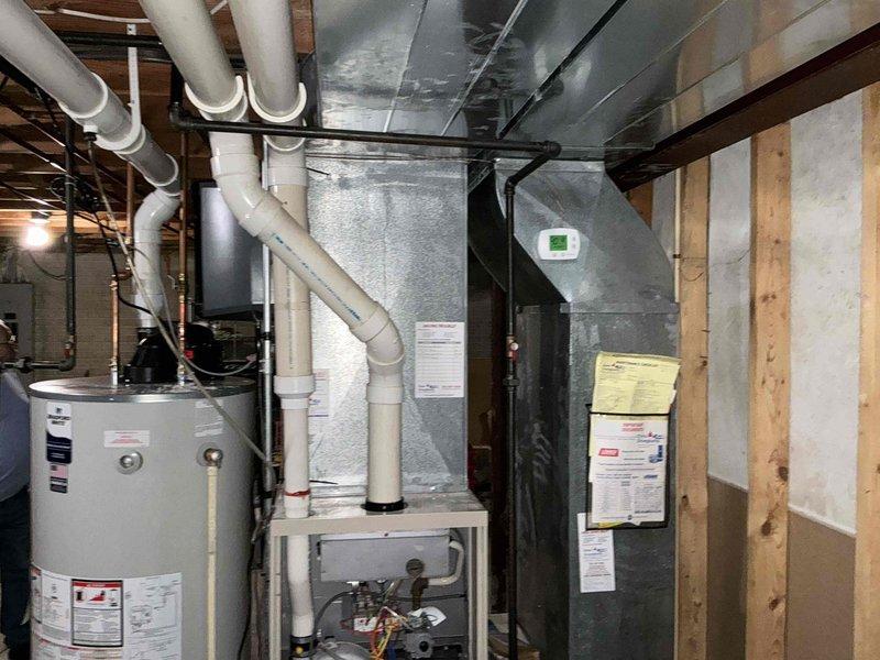 Completed visual inspection of existing Lennox furnace system in basement mechanical room. Documentation of current installation shows furnace with front panel removed to assess internal components including control board, blower motor, and wiring. Adjacent water heater and existing ductwork were also evaluated for compatibility with potential replacement system.