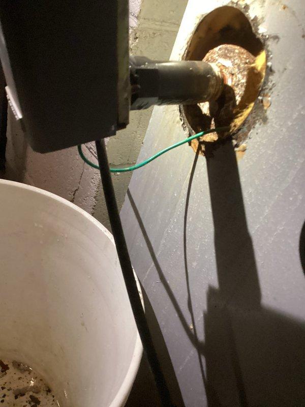 Identified and serviced severely corroded flange connection at plumbing penetration through cinder block wall. Observed significant rust deterioration around pipe entry point with compromised metal flange. Verified ground wire connection remained intact despite corrosion damage.