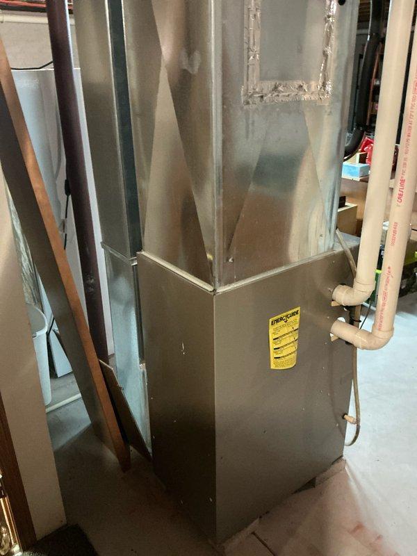 Performed comprehensive assessment of existing residential furnace system located in basement utility area. Documented current installation configuration including ductwork connections, PVC intake/exhaust venting, and electrical connectivity. Noted concrete floor condition showing cracks with drain access point and existing electrical conduit placement for replacement planning purposes.