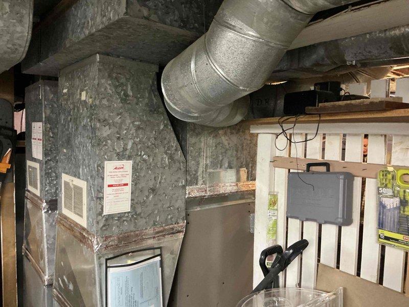 Conducted comprehensive evaluation of existing HVAC system in basement utility area, documenting condition of aging furnace unit with galvanized sheet metal casing and connected ductwork. Identified replacement requirements for primary heating unit and associated components including PVC venting system, galvanized ductwork connections, and drainage assembly with multiple valves that showed signs of normal wear.