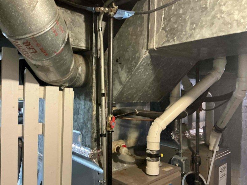 Conducted comprehensive evaluation of existing HVAC system in basement utility area, documenting condition of aging furnace unit with galvanized sheet metal casing and connected ductwork. Identified replacement requirements for primary heating unit and associated components including PVC venting system, galvanized ductwork connections, and drainage assembly with multiple valves that showed signs of normal wear.