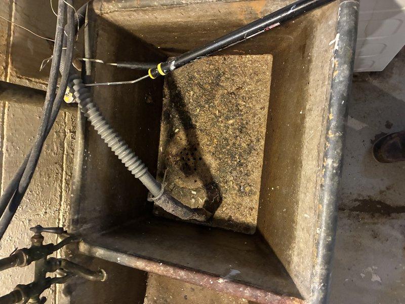 Conducted water service assessment of existing plumbing system. Inspected concrete basin containing water service connections showing significant mineral buildup and sediment accumulation. Evaluated drainage system including metal trap pipe and connected components for functionality; no active leaks detected despite aging infrastructure.