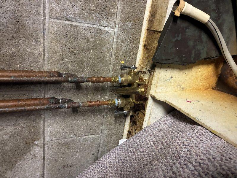 Performed inspection of residential water supply system, documenting significant copper pipe corrosion and water damage at connection points. Observed extensive oxidation with characteristic greenish-blue patina on copper pipes emerging from concrete floor, along with deterioration of surrounding materials and possible moisture-related damage. Recommended replacement of corroded supply lines and valve assemblies to prevent potential leaks and system failure.