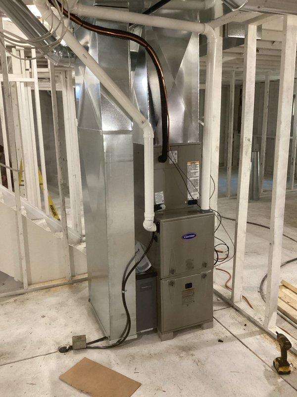 Successfully installed a complete Carrier HVAC system including indoor furnace unit with metal ductwork in basement mechanical area and outdoor condenser unit. Outdoor unit was properly mounted on a gravel bed with plastic/concrete pad foundation, with all necessary refrigerant lines and electrical connections completed. System is operational with no issues observed.