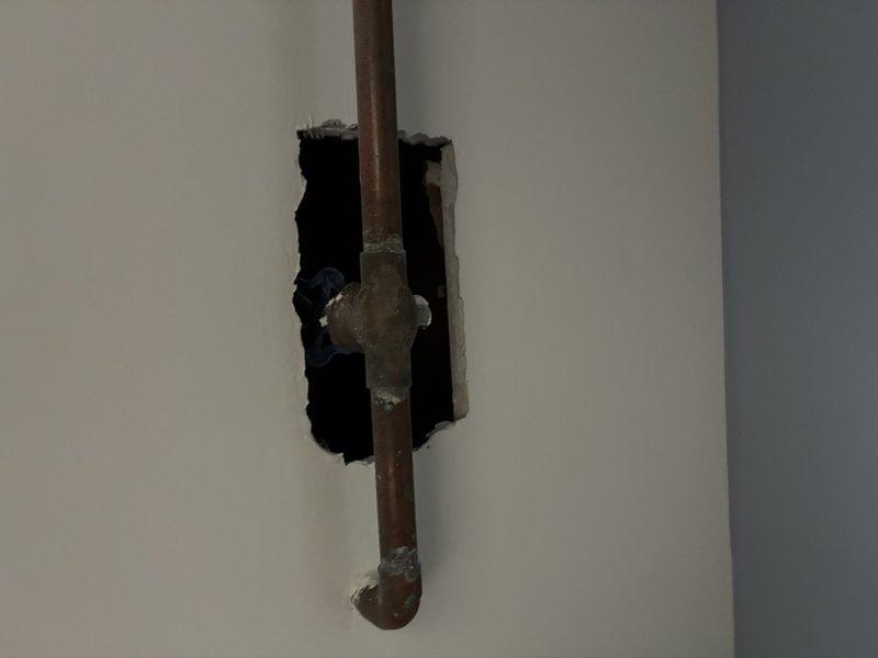 Conducted pre-paid plumbing maintenance visit to inspect wall-mounted supply line connection and exposed copper piping. Observed deteriorated drywall around supply line entry point with possible mineral buildup. Examined damaged wall section revealing copper pipe with two visible joints (coupling and elbow) showing signs of aging and potential corrosion. Documented condition of plumbing infrastructure for future reference.